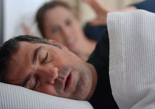 Man sleeping and snoring. Woman in the background wide awake.