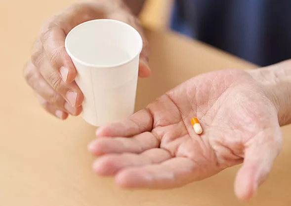 One hand holding a cup and the other hand holding a pill.